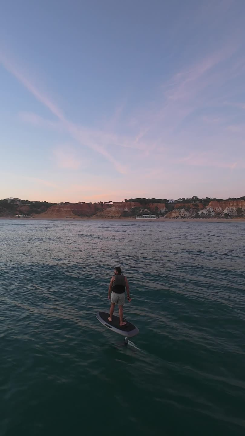 A rider on the foil at dusk, facing the red cliffs of Praia da Falésia