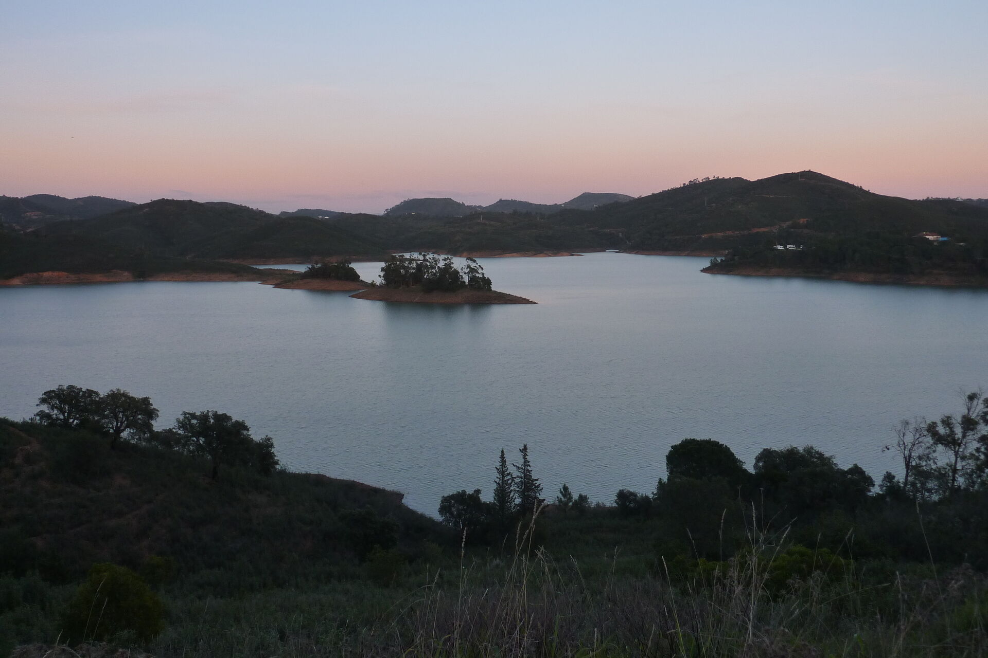 Barragem do Arade at dusk: still water, a small wooded island, and hills on every side